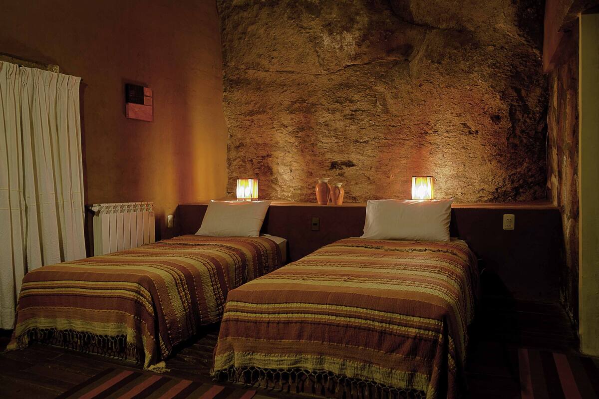 Quarto com duas camas, parede de pedra, radiador e janela com cortinas.