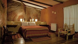 A bedroom with a wooden floor, a bed with a striped blanket, bedside tables with lamps, a radiator, and a wooden chair.