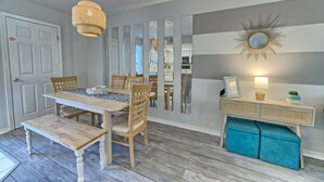 Un comedor con una mesa y sillas de madera, un banco, una lámpara colgante y un espejo fijado a la pared.