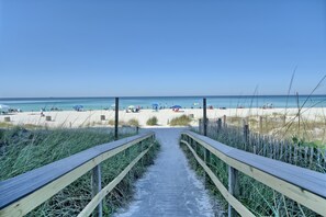 A wooden boardwalk leading to a beach with umbrellas and beach chairs. - Heart of PCB! Walk to Beach, Golf Cart Included, Steps to Pool & Mini Golf! (Panama City Beach)