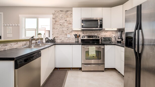 A modern kitchen with white cabinets, a stainless steel refrigerator, a microwave, an oven, and a dishwasher. - Ranch Guest House (Tucson)