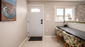 A room with a white door, a window with a view, a cactus-themed chair, and a wall-mounted picture of a river. - Ranch Guest House (Tucson)