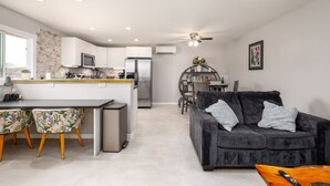 A modern kitchen with a central island, a dining area with a dark grey sofa, and a ceiling fan. - Ranch Guest House (Tucson)