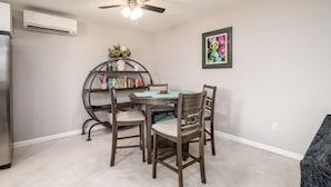 A dining area with a table and four chairs, a ceiling fan, an air conditioning unit, a bookshelf, and a framed picture on the wall. - Ranch Guest House (Tucson)