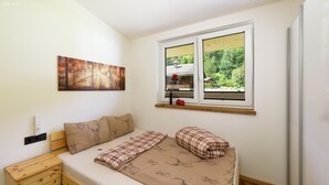 Un dormitorio con una cama, una mesita de noche, un ventanal con vistas a la vegetación y un cuadro en la pared.