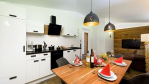 Una cocina moderna con armarios blancos, una mesa de comedor de madera dispuesta con servilletas rojas, copas de vino y una botella.