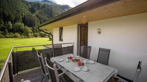 Una mesa de comedor en un balcón con vistas a la montaña, sillas para exteriores y una terraza de madera.