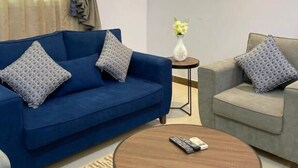 Un salon moderne avec un canapé bleu, un canapé gris, une table basse ronde et une petite table d’appoint sur laquelle est posé un vase.