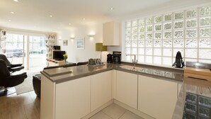 A modern kitchen with a large island, built-in appliances, and a view through a frosted window. - The Point (St Ives)