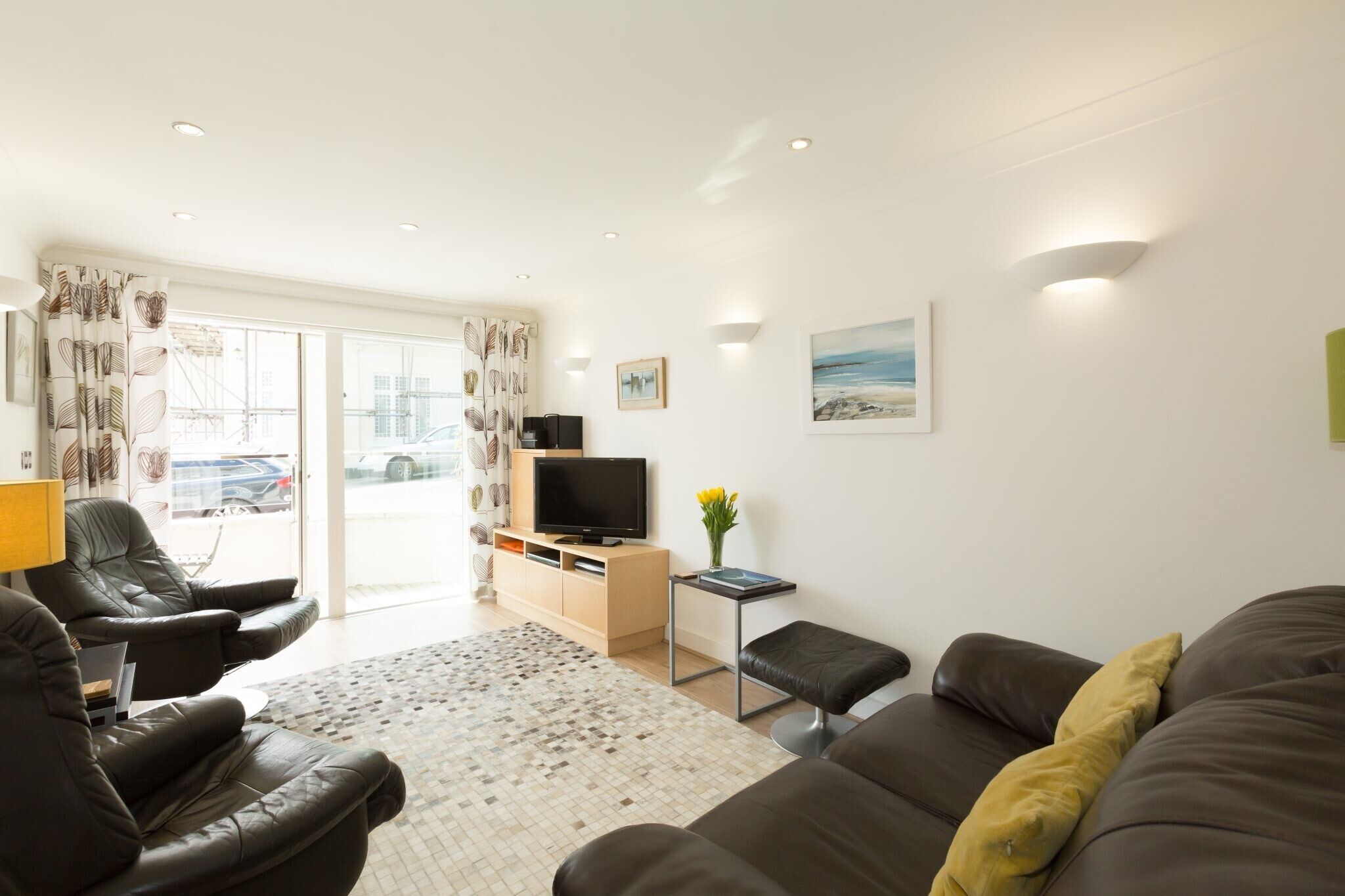 A modern living room with a sofa, armchairs, a TV, and a view of the outside.
