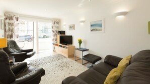 A modern living room with a sofa, armchairs, a TV, and a view of the outside. - The Point (St Ives)