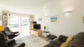 A modern living room with a sofa, armchairs, a TV, and a view of the outside.