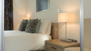 A neatly arranged hotel room with a bed, bedside lamps, a nightstand, and a wall-mounted artwork. - The Point (St Ives)