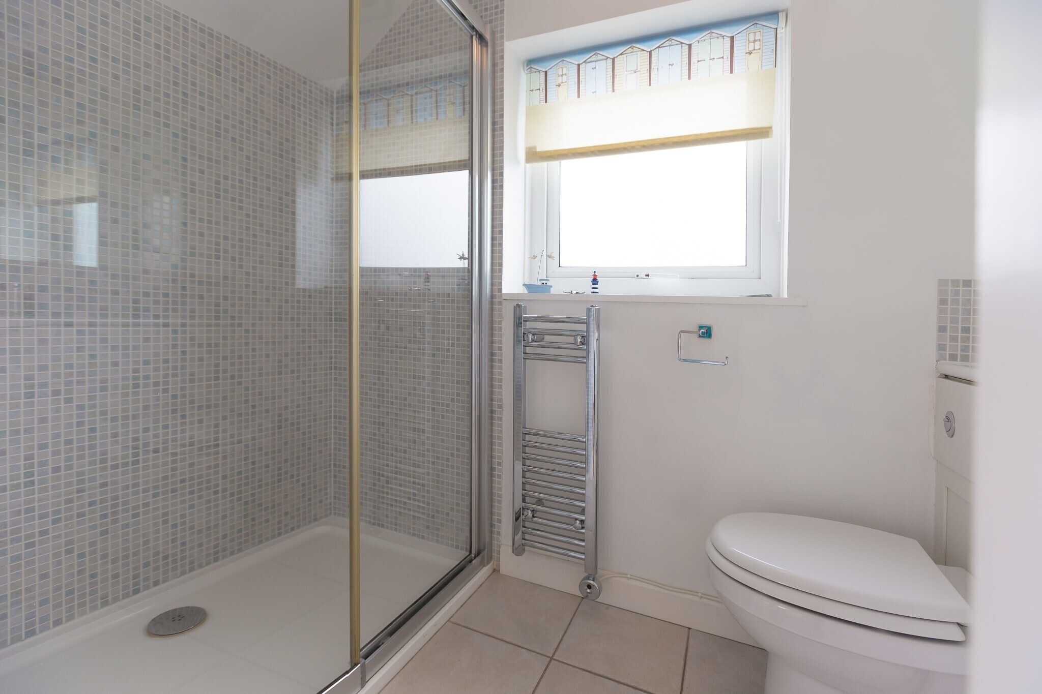 Ein Badezimmer mit Glasdusche, weißer Toilette und Fenster mit Blick auf Häuser.