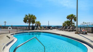 A swimming pool with a curved edge, surrounded by lounge chairs and palm trees, with a clear view of the ocean in the background. - ⭐Newly Renovated, Beachfront-1BR Sunbird 309E⭐ (Panama City Beach)