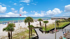 A beach view with a wooden deck, palm trees, and beach umbrellas. - ⭐Newly Renovated, Beachfront-1BR Sunbird 309E⭐ (Panama City Beach)