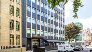 A modern building with a mix of brick and glass facades, a white van parked in front, and a tree to the right. - Stunning Modern Apartment in the Heart of Holborn (London)