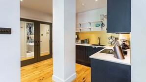 A modern kitchen with a central island, dark cabinetry, and a wooden floor. - Stunning Modern Apartment in the Heart of Holborn (London)