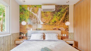 A hotel room with a large bed, white linens, a waterfall mural on the wall, and a window with a view of trees. - PF42 Excelente Casa 4 Quartos (Mata de São João)