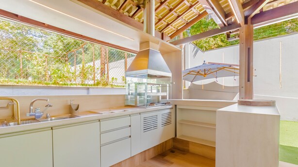 A modern kitchen with a large window, wooden ceiling, and a built-in grill. - PF42 Excelente Casa 4 Quartos (Mata de São João)