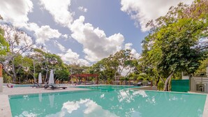 A swimming pool with lounge chairs and umbrellas, surrounded by trees and a clear sky. - PF42 Excelente Casa 4 Quartos (Mata de São João)