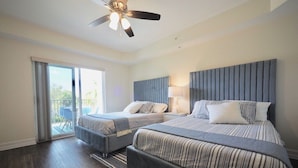 A hotel room with two beds, a ceiling fan, a sliding glass door to the balcony, and a small table with chairs. - ★Cozy Beach Escape★ 0.9 miles from Clams Pass Beach ! (Naples)