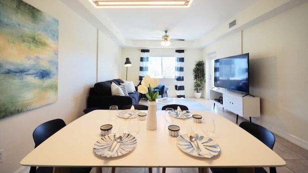A modern living room with a dining area, a flat-screen TV, and a large abstract painting. - ★Cozy Beach Escape★ 0.9 miles from Clams Pass Beach ! (Naples)