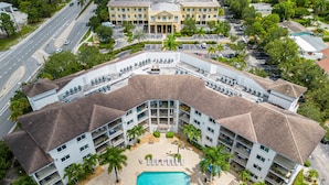 A multi-story hotel with a swimming pool, multiple balconies, and a parking area. - ★Cozy Beach Escape★ 0.9 miles from Clams Pass Beach ! (Naples)