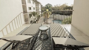 A balcony with two tables and a chair, a view of a building, and a pool in the background. - ★Cozy Beach Escape★ 0.9 miles from Clams Pass Beach ! (Naples)