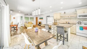 A modern kitchen with white cabinets, a central island, and a dining area with a wooden table and chairs.