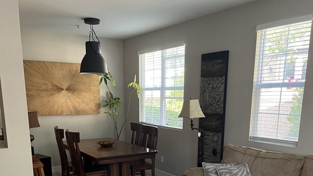 A living room with a dining table, chairs, a sofa, a coffee table, and two windows with blinds.