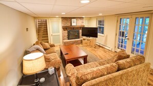 Un salon avec une cheminée, un canapé, un téléviseur et une vue sur l’extérieur grâce aux portes vitrées.
