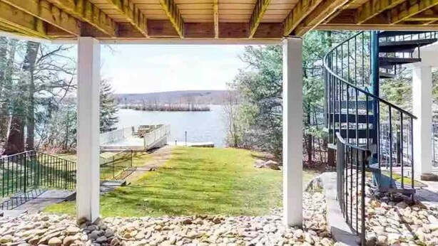 Un espace extérieur abrité offrant une vue sur un lac, une pelouse verdoyante et un escalier en colimaçon.