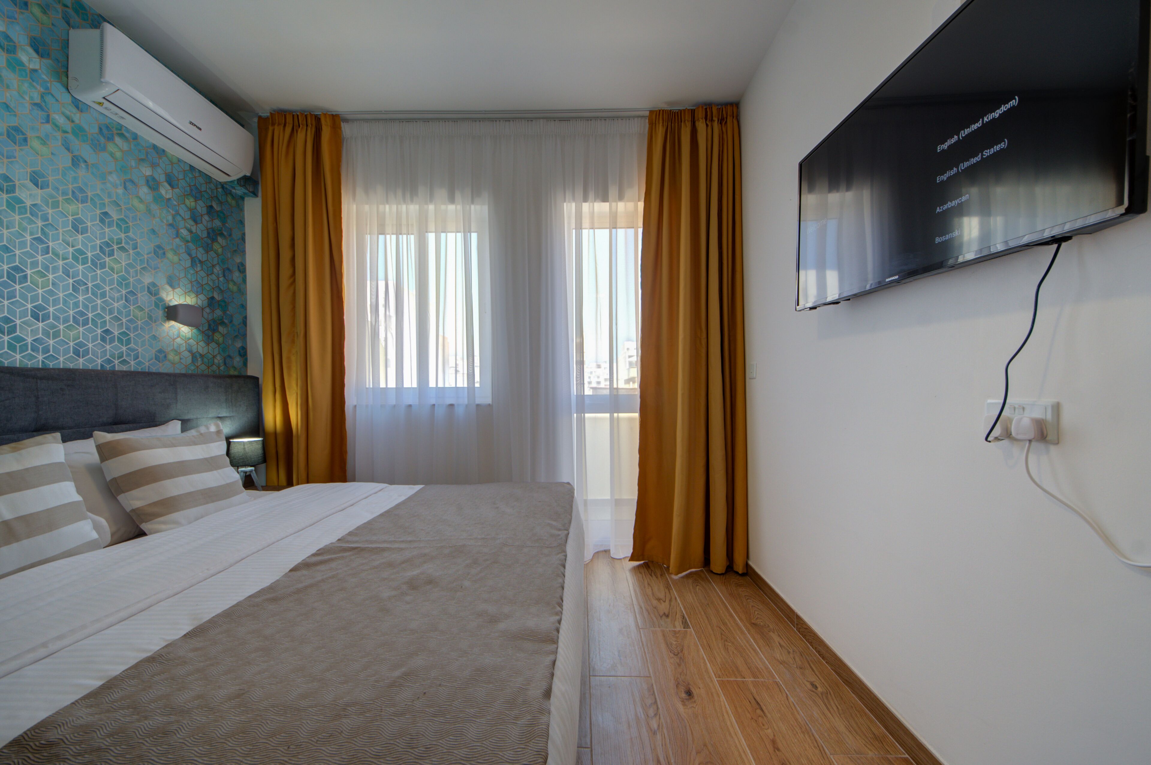 Habitación de hotel con cama, televisor montado en la pared y ventana con cortinas.