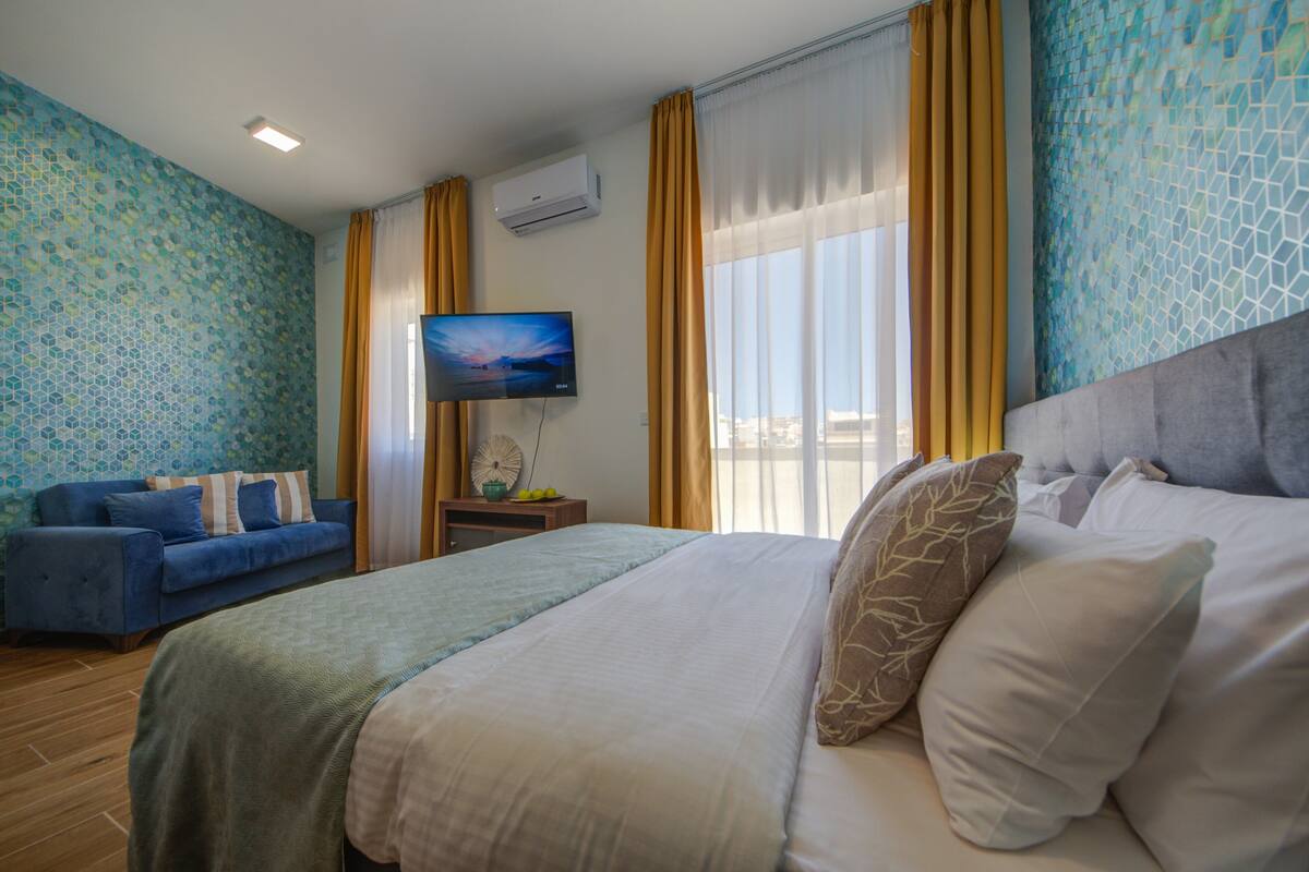 Ein Hotelzimmer mit einem Bett, einer Couch, einem Fernseher und einem Fenster mit Vorhängen.