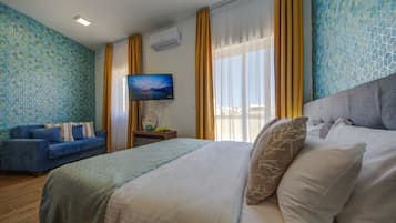 A hotel room with a bed, a sofa, a TV, and a window with curtains.