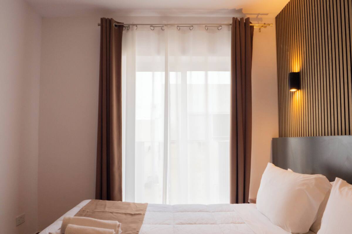 Ein Hotelzimmer mit Bett, Vorhängen, Kopfteil und Wandlampe.