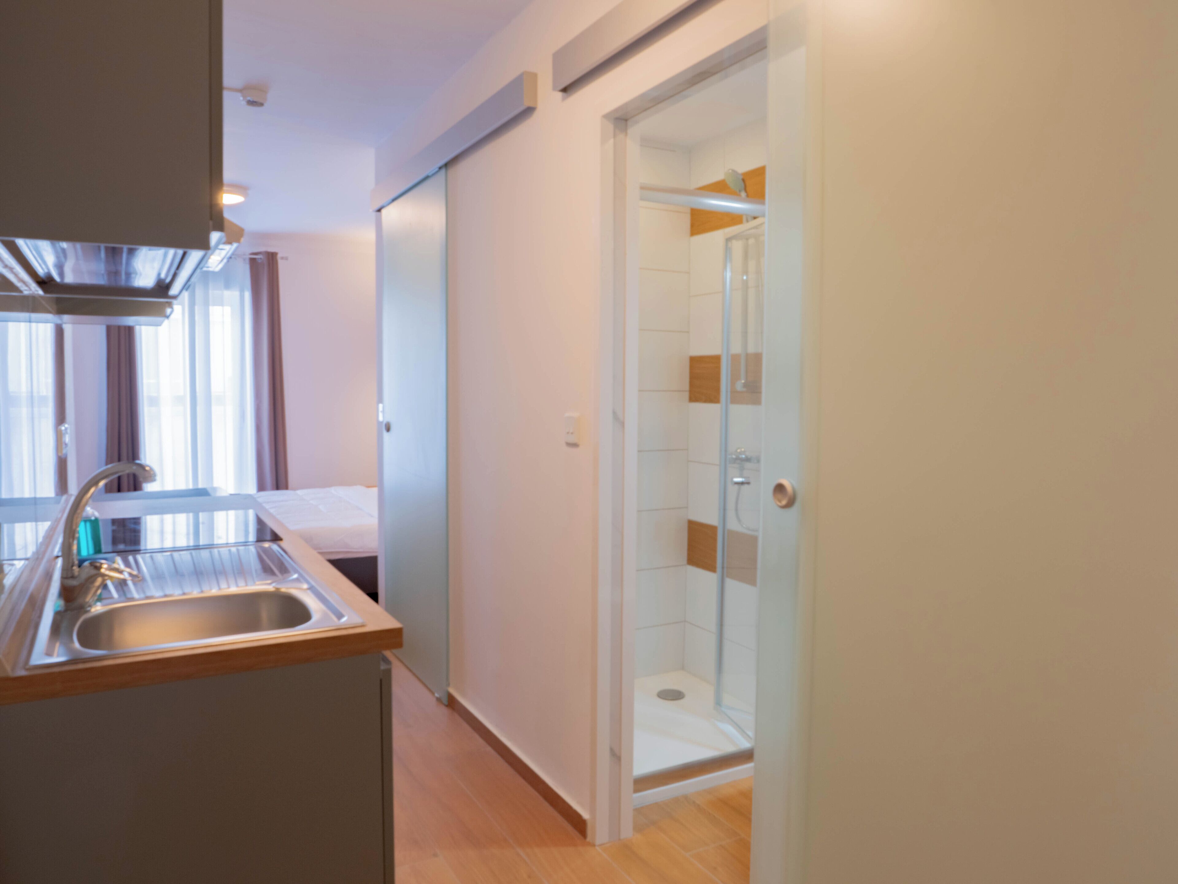 Moderni hotellihuone, jossa on pieni keittiö, suihku ja sänky.