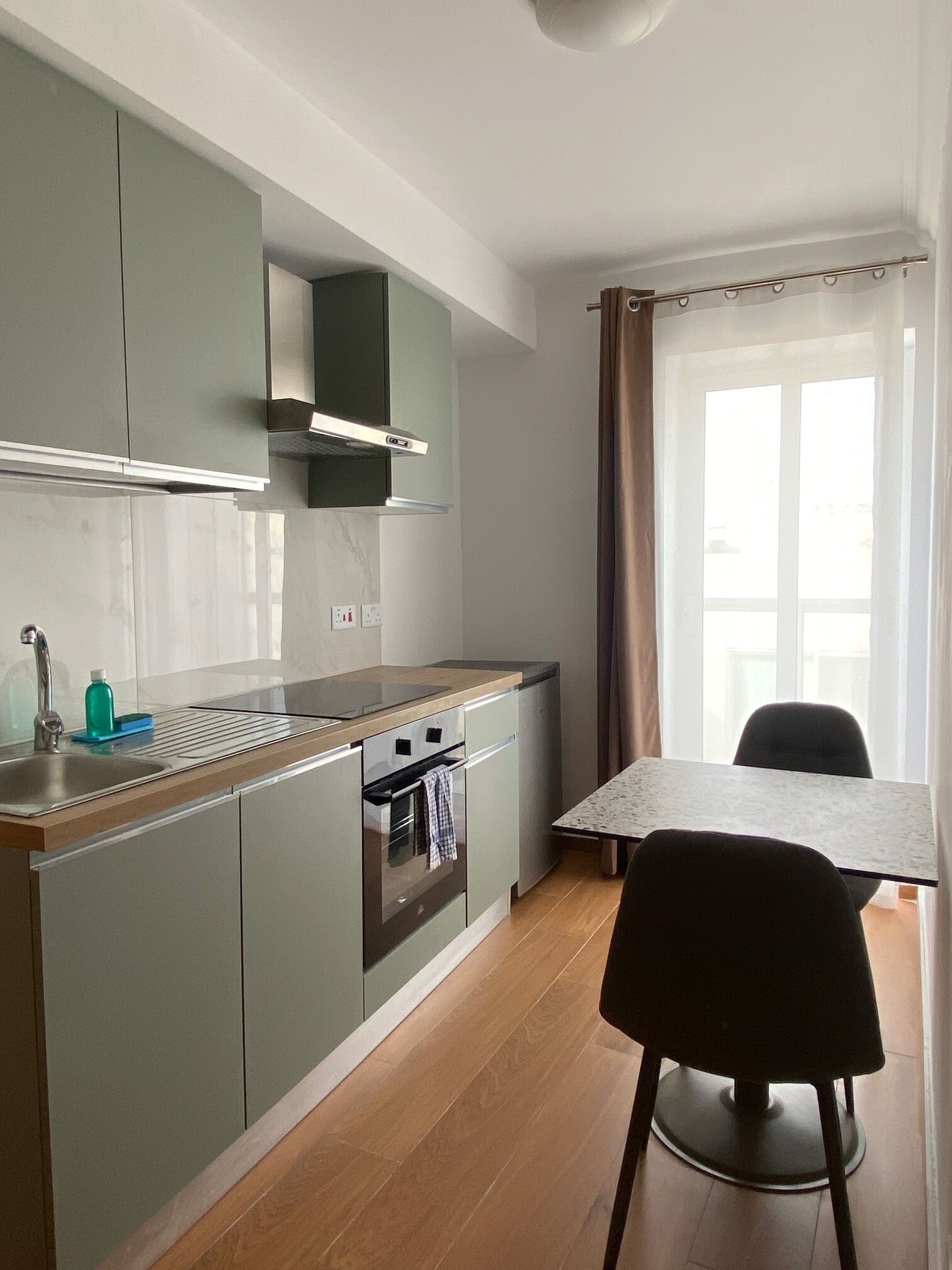 Une cuisine compacte dotée d’un four encastré et d’un coin repas avec une table et des chaises.