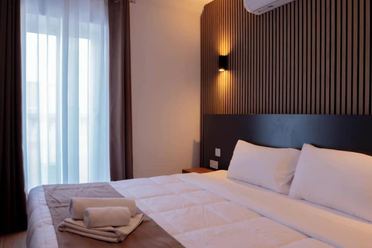 Une chambre d’hôtel avec un lit, une table de chevet, un climatiseur fixé au mur et une fenêtre avec des rideaux.