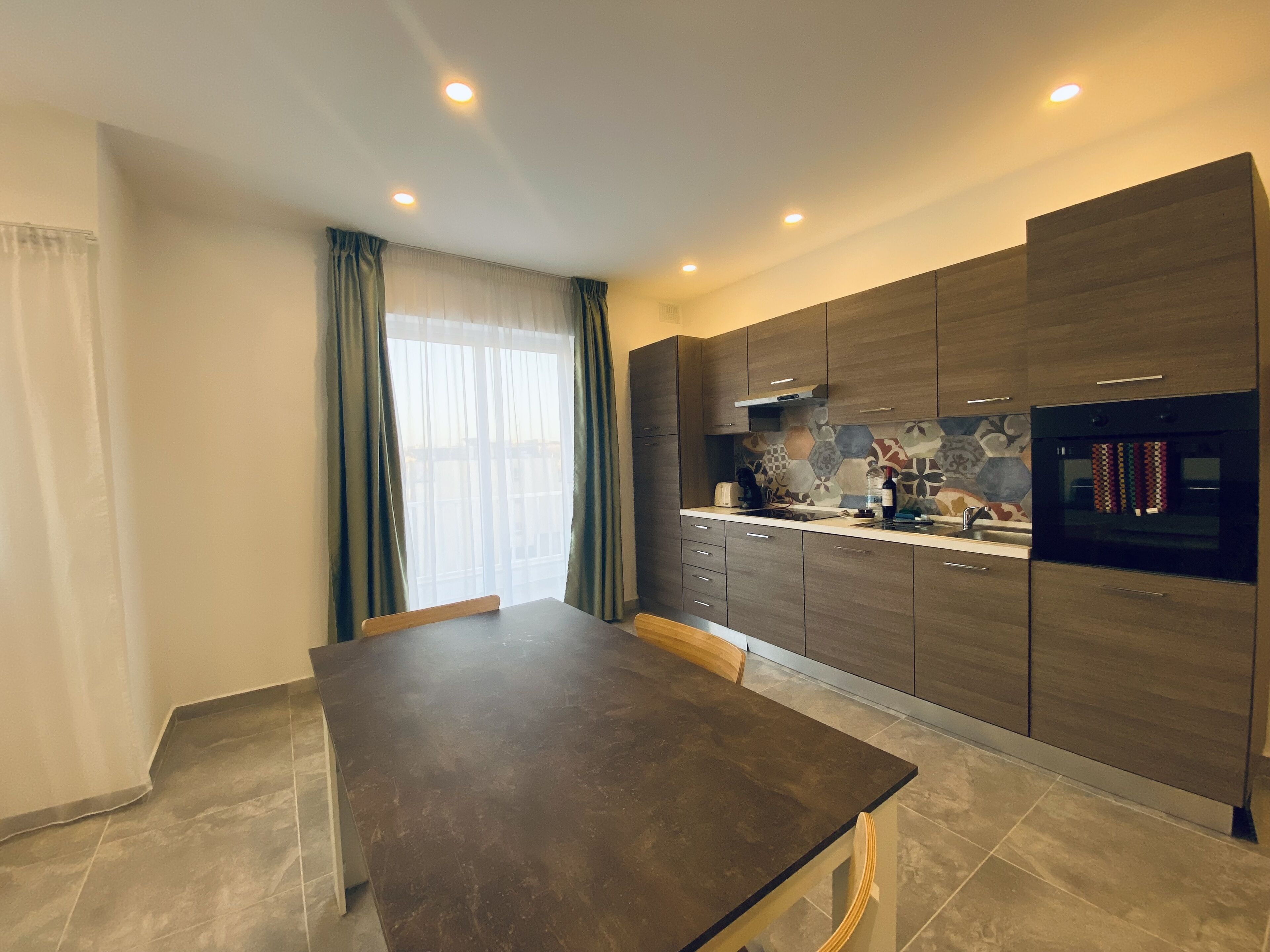 A modern kitchen with dark wooden cabinets, a black countertop, and a built-in oven.