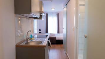 A compact kitchen with a sink, a stove, and a small countertop. A bed is visible in the background, and the room has a sliding door.