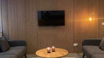 A modern living room with a flat-screen TV mounted on a wooden wall, two sofas, a round coffee table, and a carpeted floor.