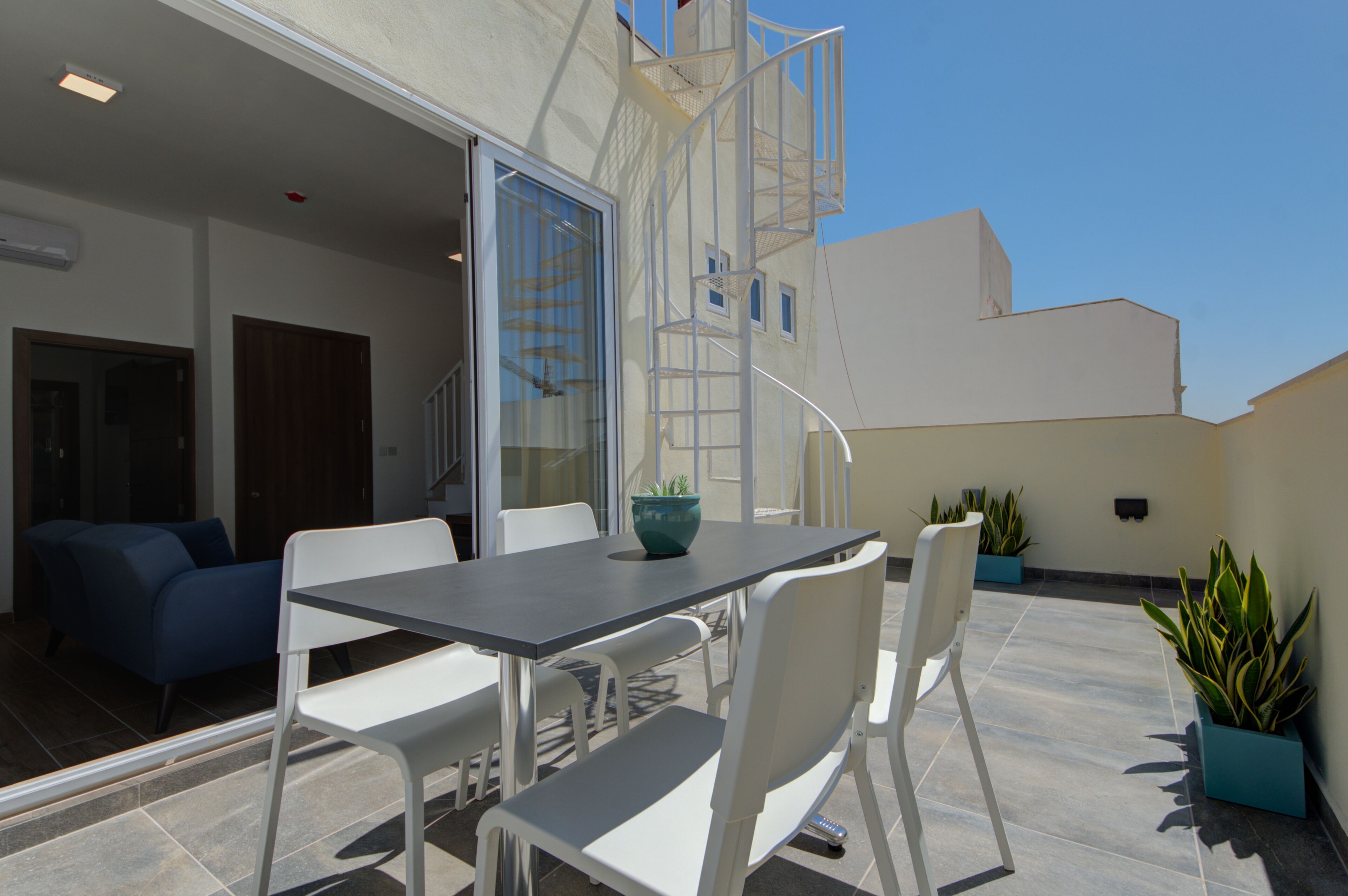 Eine Terrasse im Freien mit Tisch, Stühlen, einer Treppe und Blumentöpfen.