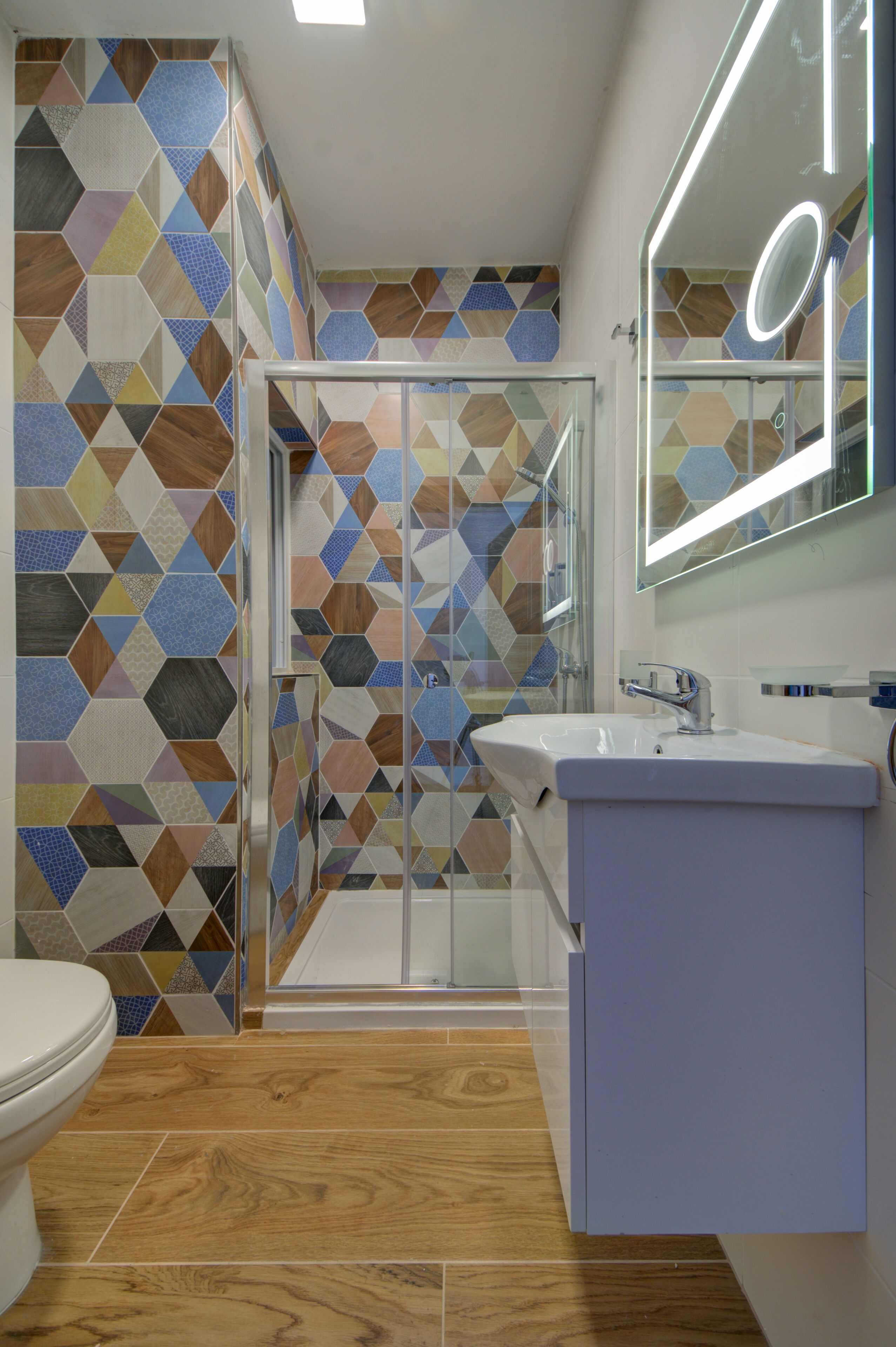 A modern bathroom with a geometric tile backsplash, a glass shower enclosure, and a white sink with a mirror.