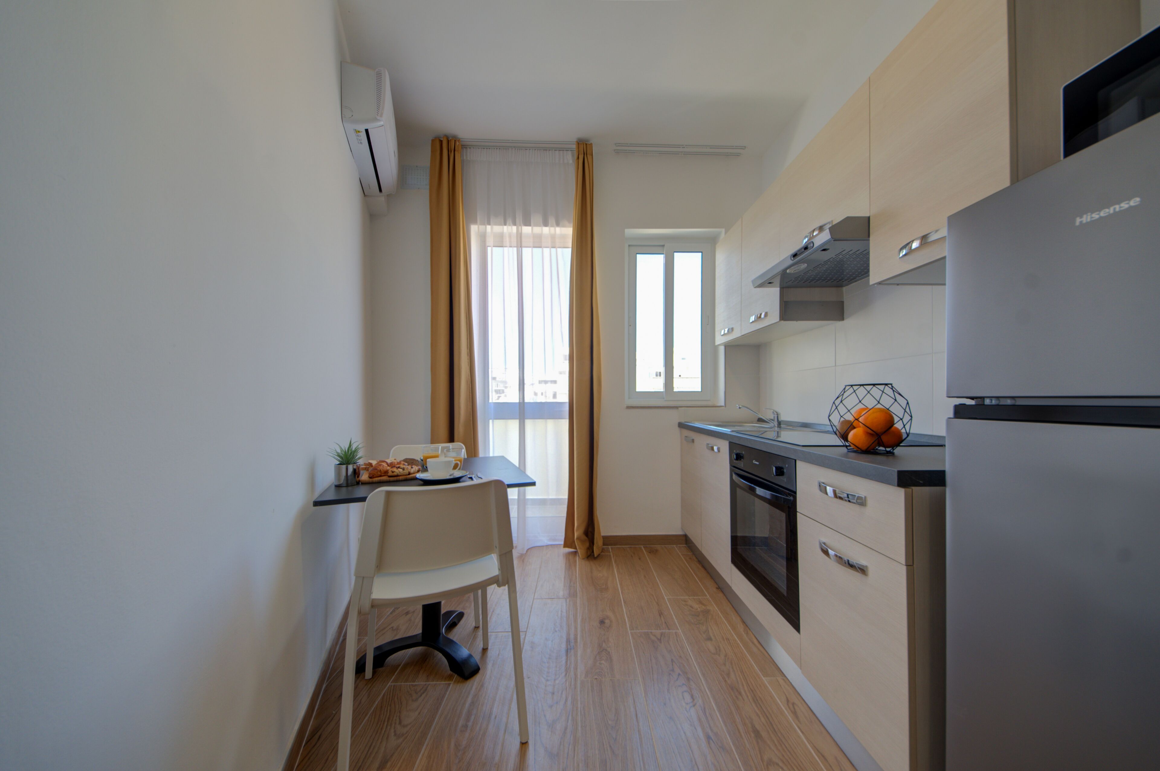 Una cocina compacta con comedor, refrigerador y ventana con cortinas.