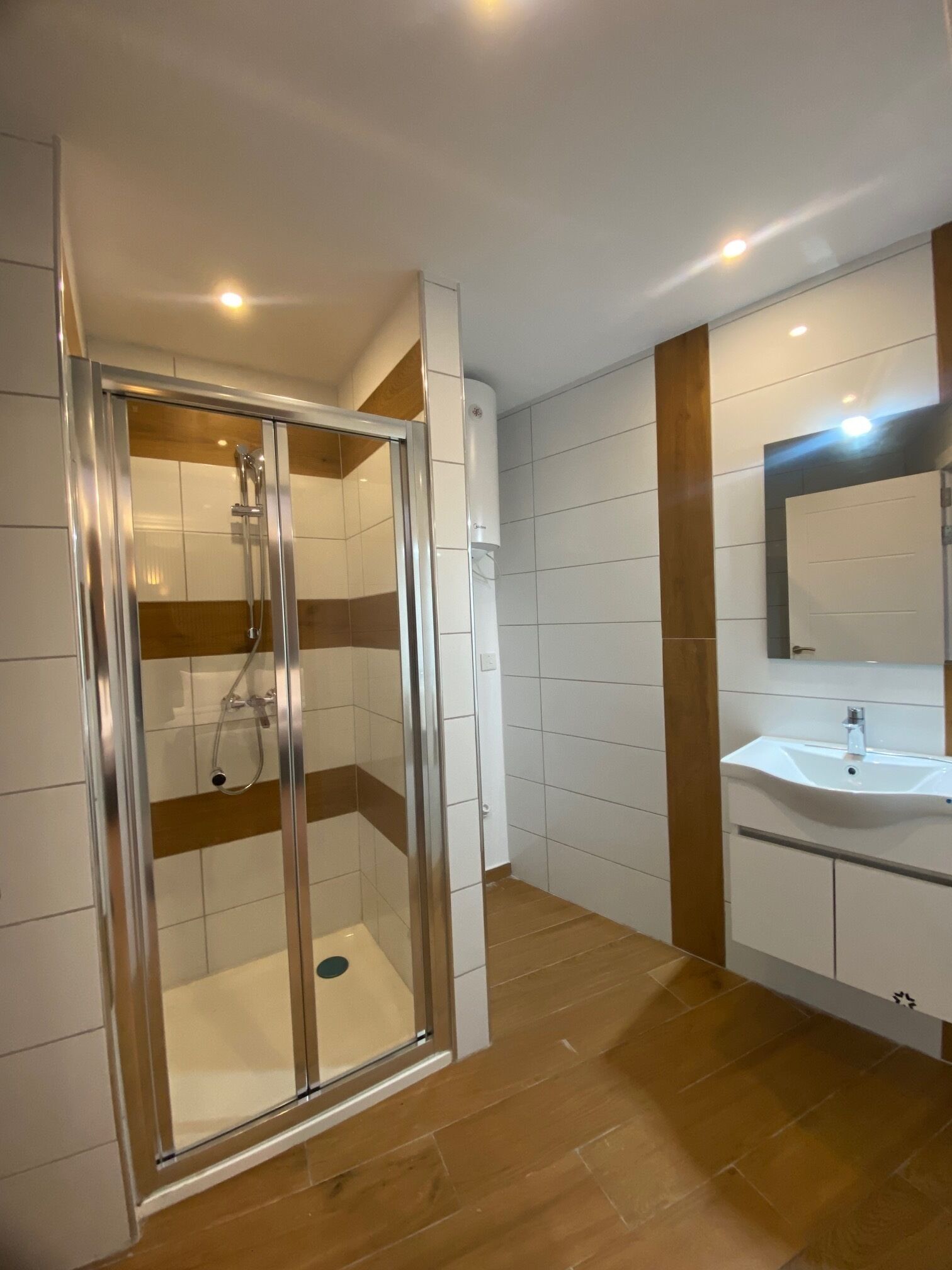 A modern bathroom with a glass-enclosed shower, white tiles, and wooden flooring.