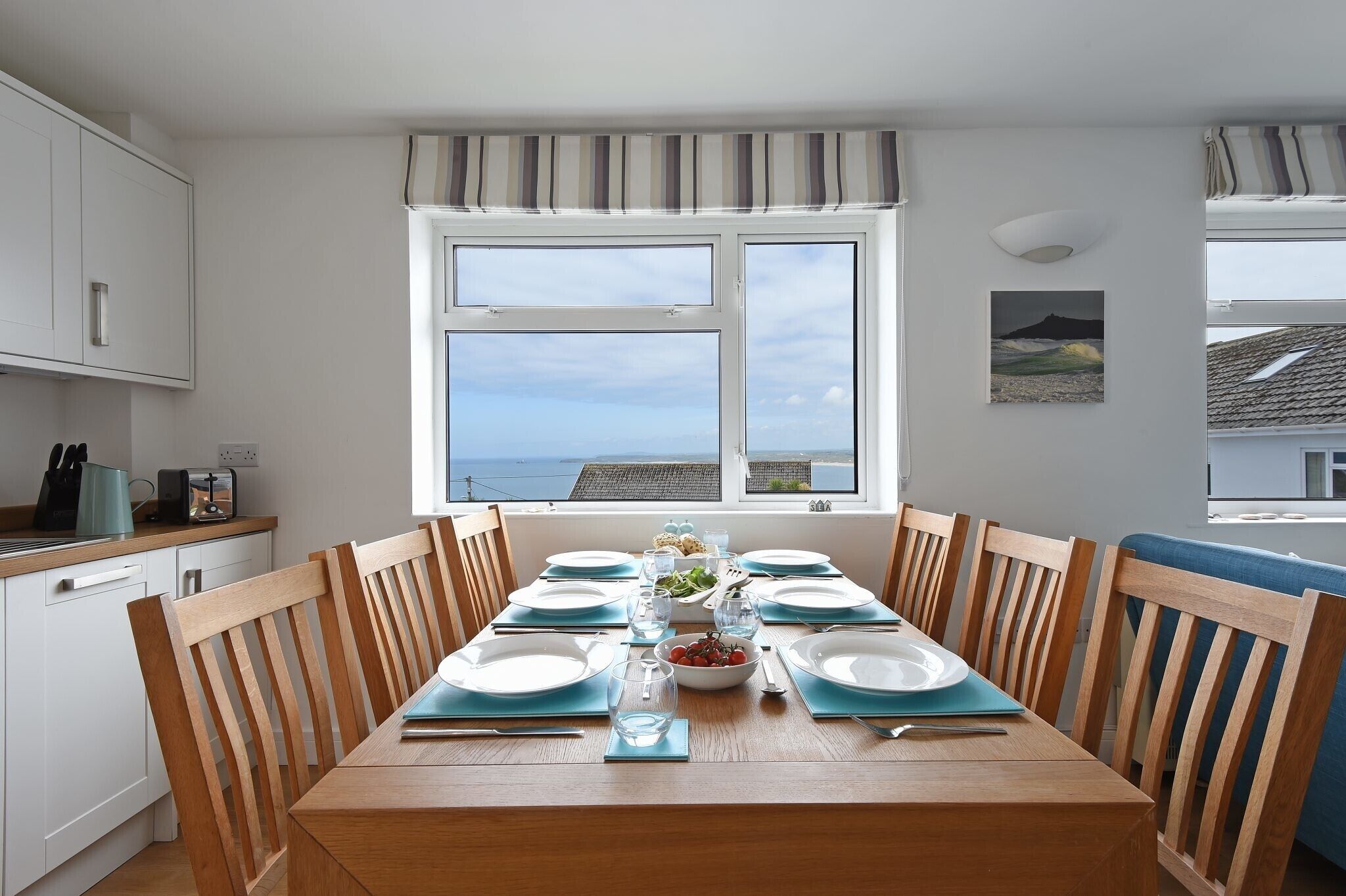 A dining area with a table set for four, a window with a view, and a kitchen area with white cabinets and a blue countertop.