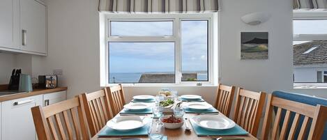 A dining area with a table set for four, a window with a view, and a kitchen area with white cabinets and a blue countertop.
