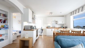 Un espace de vie et de salle à manger moderne, à aire ouverte, avec une cuisine, un plancher en bois et une grande fenêtre offrant une vue dégagée.